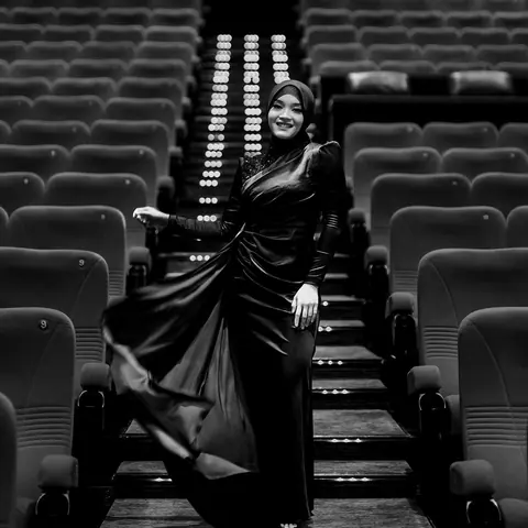 A woman in a dark satin dress posing on the steps of an empty cinema, in black and white