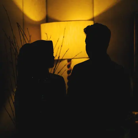 The couple of the N and I engagement in silhouette, facing each other before a glowing lampshade