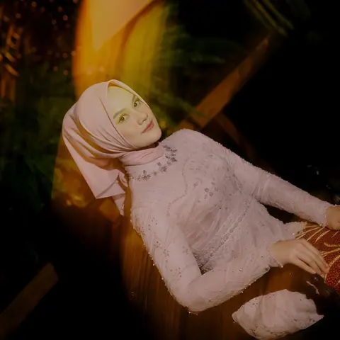 The bride-to-be in a pink hijab and beaded pink dress, reclining in warm light