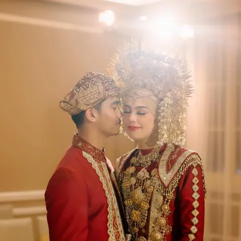 Nadin and Muiz in red and gold, the bride in a tall gold headdress, the groom kissing her temple