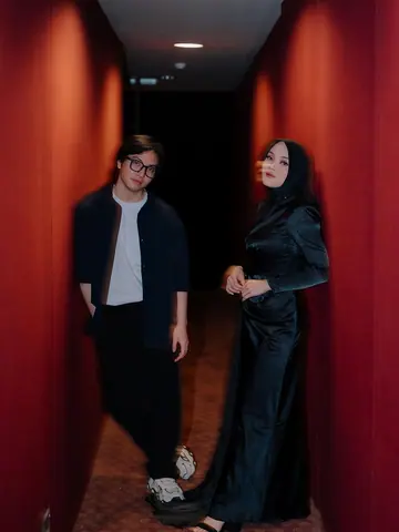 A couple standing between red curtains in a dark corridor