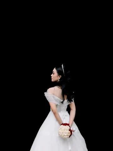 A bride in a white off-shoulder gown and tiara, her back turned, holding red and white roses behind her