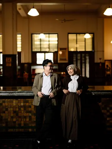 A couple in a high old hall with tiled counters, tall windows and hanging lamps