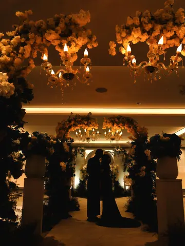 A couple in silhouette under arches of flowers and candle chandeliers