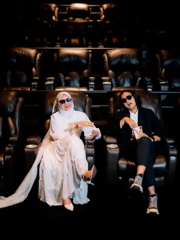 A prewedding couple in sunglasses with popcorn in the reclining seats of a cinema