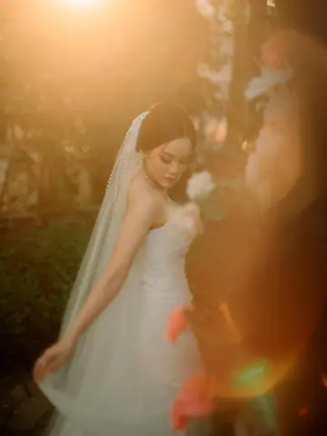 A bride in a long veil and strapless gown, lit gold by the low sun